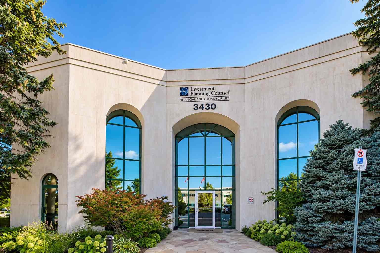 The exterior entrance of 3430 South Service Rd. in Burlington, Ontario — a light stone professional building with arched windows and landscaped greenery